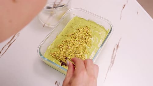 Top Down View Of Female Hands Adjusting Pistachio Topping On Green Cream Layer Of Homemade Tiramisu