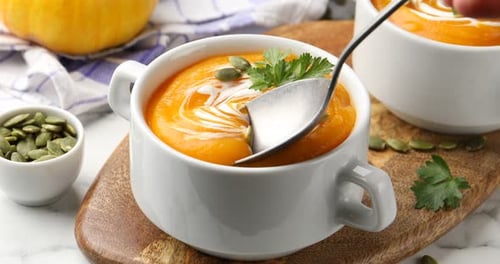 Frau nimmt leckere Kürbiscremesuppe mit Löffel aus der Schüssel am Tisch, Nahaufnahme