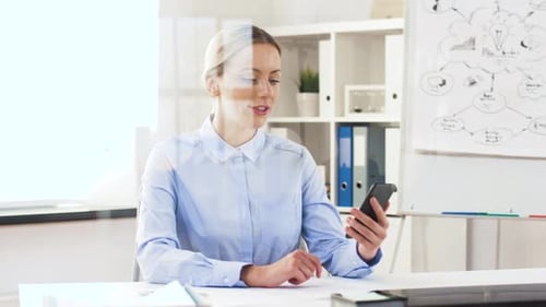 Happy businesswoman in office having video call on smartphone through glass