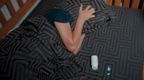 Person Covering Head in Bed with Pills Nearby