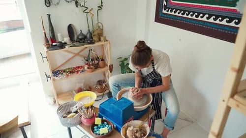 Une potière vêtue d'un jean et d'un tablier travaille sur un tour de potier et fabrique un pot en céramique en argile