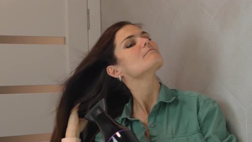 Woman Drying Hair with Hair Dryer in Bathroom