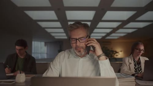 Empresário de meia idade falando no telefone e trabalhando no laptop no escritório