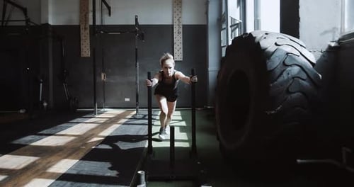 Young Beautiful Athletic Caucasian Woman Pushing Training Sled Towards Camera Exercising in Hardcore
