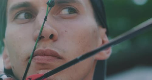 Slow motion close up of young man with professional equipment is practising archery with a bow in