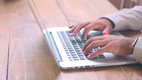 Close Up Hands of Man Typing Text on Laptop Keyboard Located on Wooden Table