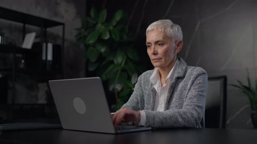 Smiling Senior Businesswoman Working on Laptop in Modern Office