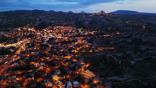 Aerial Dusk View of Illuminated Town Nestled Against Majestic Mountains