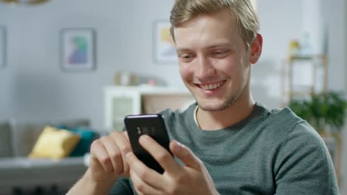 Smiling man uses smartphone in modern living room