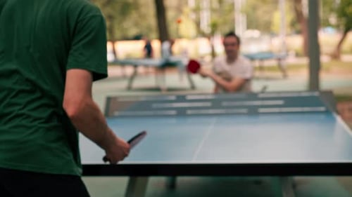 A man in a wheelchair plays table tennis ping pong with his friend in a city park outdoor activity