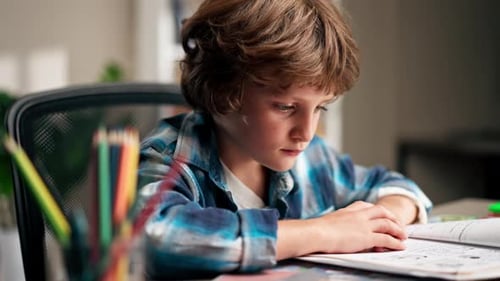 Close Up in the Children's Room a Schoolboy in a White Sweater and a Blue Checkered Shirt at a Desk