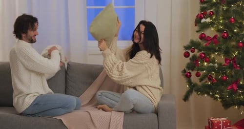 Playful Couple Enjoying Pillow Fight Near Christmas Tree