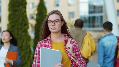 Nice Caucasian Female Student Holding Her Bag and Books Waiting for Lectures Standing Near Campus