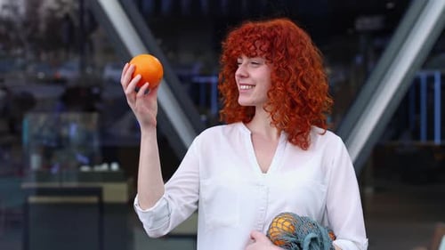 Young Woman with Red Hair Holding an Orange in the City