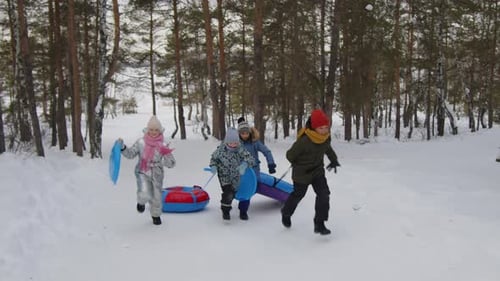 Fröhliche Kinder, die im Winter mit Schneeröhren und Untertassen den Hügel hinauf rennen