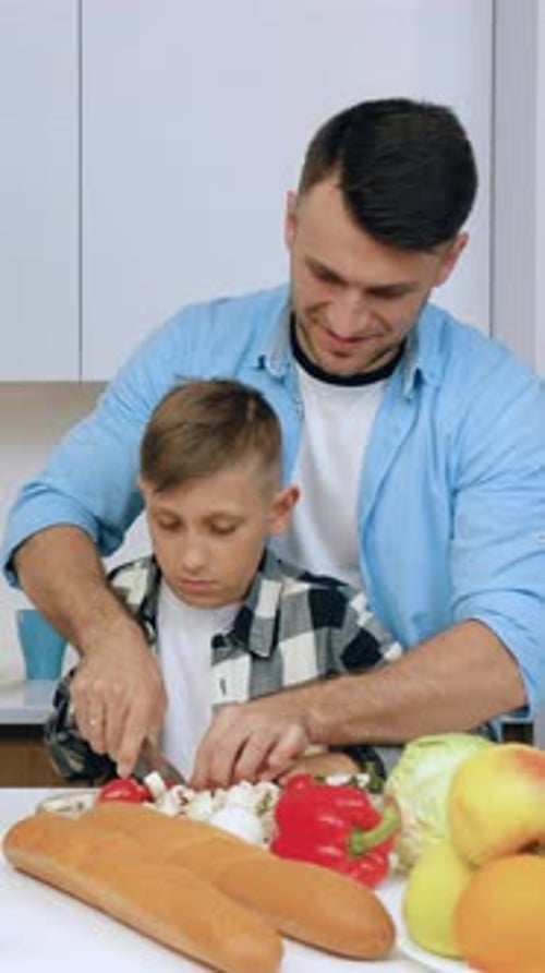 Dad Teaches Son to Chop Vegetables in Kitchen