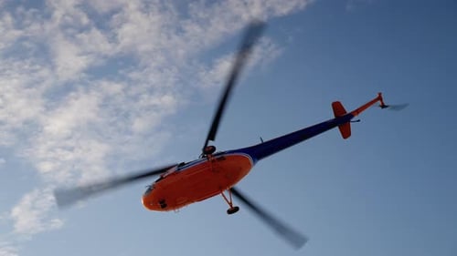 Bright Orange Helicopter Flying Through Cloudy Blue Sky
