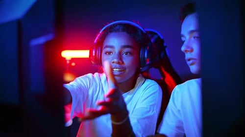 White boy and black girl teens in headsets discussing while playing video games in video game club w