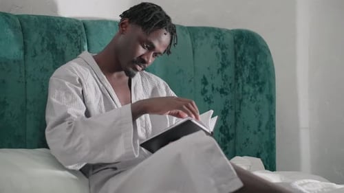Man in Robe Reads Book in Bed