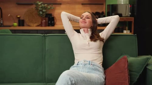 Young Brunette Woman Resting at Home Sitting on a Green Sofa with Her Hands Behind Her Head A Young