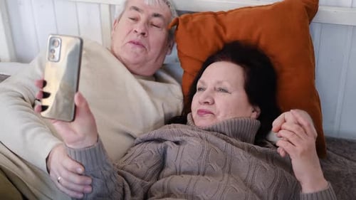 Affectionate Senior Couple Lying on Bed Looking at Phone