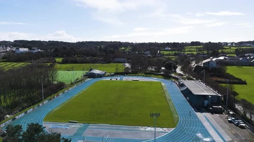 Sports stadium flight over stadium, not in use showing field, track and grandstand on bright sunny d