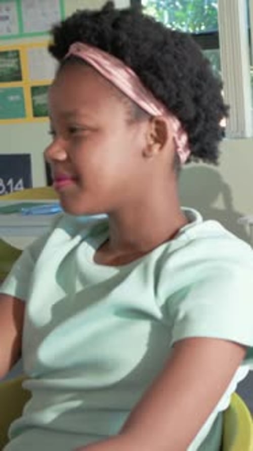 Vertical video: Teacher calling student in green top lowering arm, looking toward classroom window