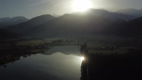 Aerial view from right to left over an alpine lake early in the morning. Sun shinning over the Mont