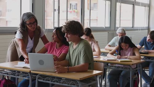 High School Female Teacher Helping Diverse Young Students in Classroom