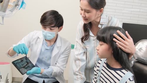 Asian male pediatric dentist explains teeth X-ray to a girl in a dental clinic.