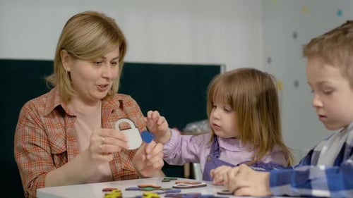 Teacher Guides Children Assembling Puzzle in Classroom