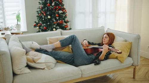 Woman Relaxing on Couch, Playing Guitar at Christmas