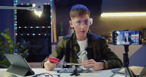 Boy Vlogger hace transmisiones en línea con un teléfono inteligente y estudia electrónica y cables de soldadura