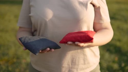 Una mujer irreconocible sostiene diferentes bolsas de cornhole en sus manos en un césped soleado