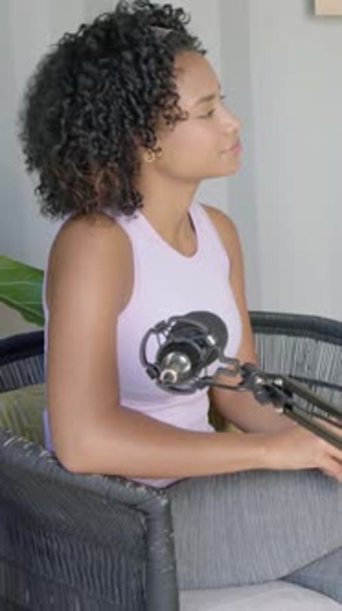 Vertical video: Camera pulling back revealing woman in lilac tank adjusting hands for podcast, mic