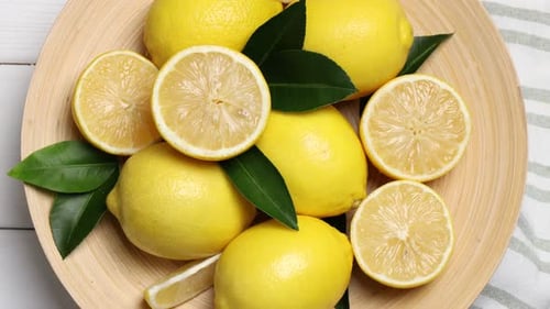 Ripe lemons and leaves spinning on white wooden table, top view