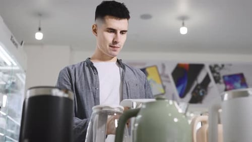 A Man in an Electronics Store Chooses an Electric Kettle with WiFi and Automatic Functions