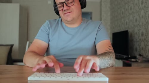 Man Typing at Desk Wearing Headphones and Glasses