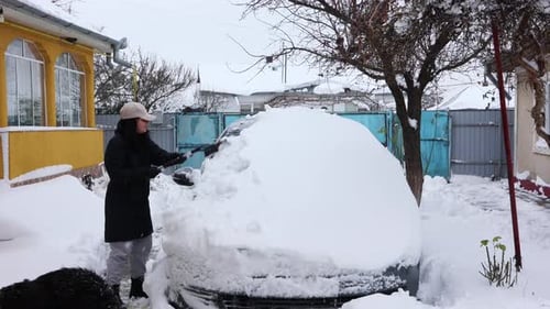 Woman Removing Heavy Snow From Car Windshield
