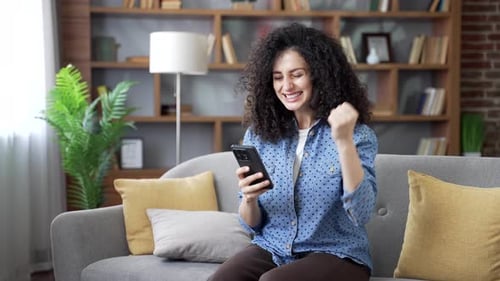 Woman Sitting on Couch, Looking at Smartphone, Smiling