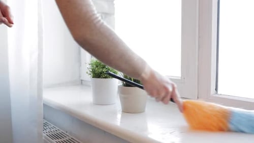 Man dusting window sill with colorful duster