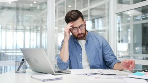 Businessman is tired of doing paperwork and doing tasks sitting at workplace in business office.