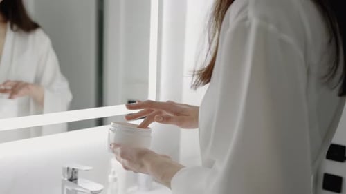 Woman Applies Moisturizer in Bright Minimalist Bathroom