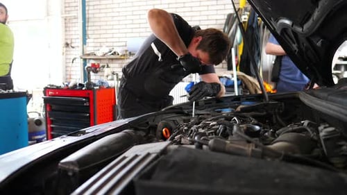 Young Repairman Working Under Hood of Vehicle at Service Professional Auto Mechanic Fixes Engine of
