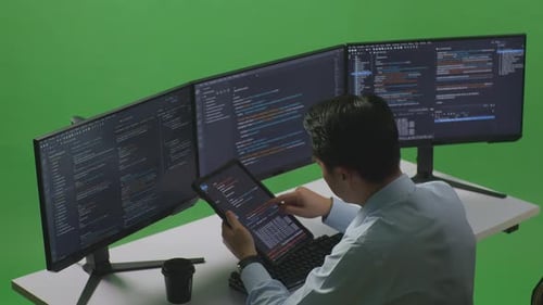 Asian Man Working With Tablet While Write Code With Multiple Computer Screens In Green Screen