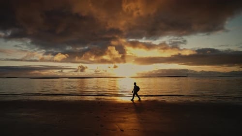 Silhouette of Young Man Walking on the Sandy Beach at Sunset Enjoying Vacation