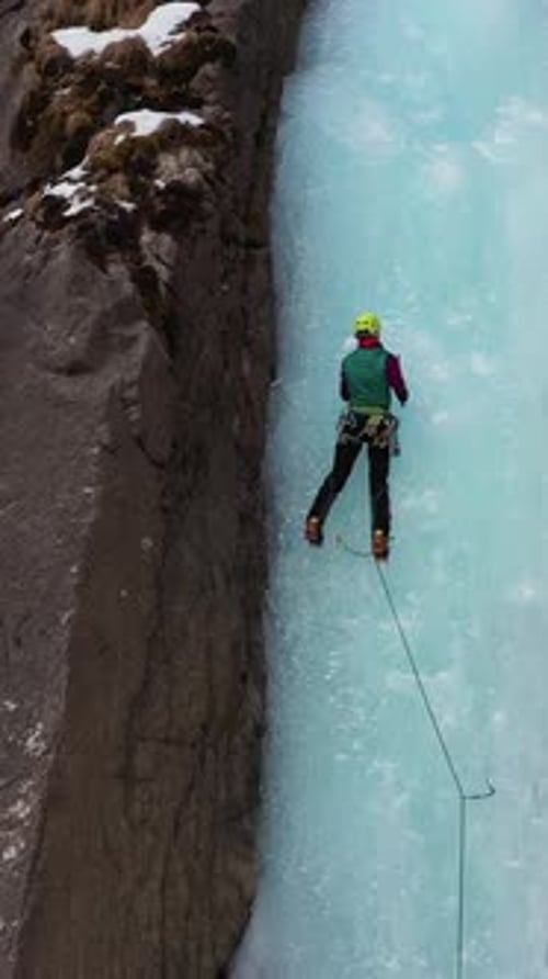 Frau führt auf Eiseis und klettert auf einem gefrorenen Wasserfall Vertikales Video aus der Luft