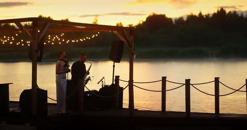 Dúo de jazz siluetted tocando en el muelle junto al lago al atardecer