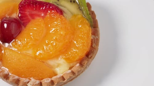 Pasteles giratorios con frutas sobre fondo blanco.