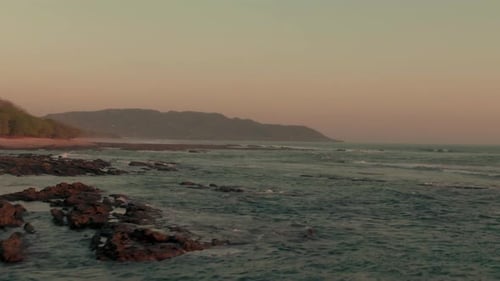 Aerial low parallax shot of swell breaking on empty beach in Costa Rica twilight